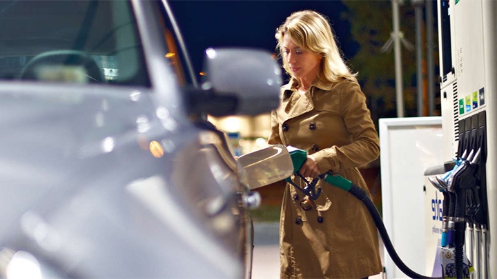 Under kraftig kuppelbelysning fra Philips fyller en kvinne opp tanken på bilen sin på en bensinstasjon.
