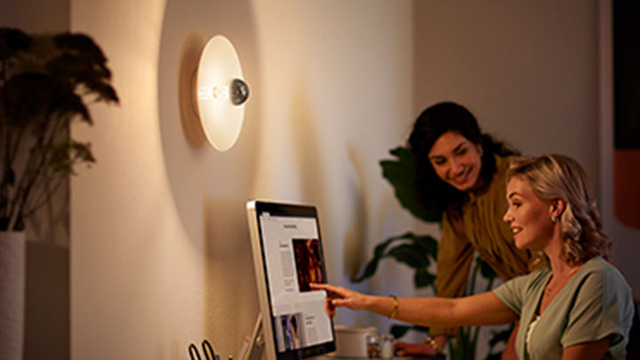 Kvinne jobber på PCen ved siden av en veggmontert Philips LED