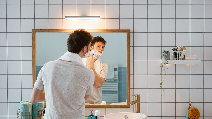 Mann barberer seg foran et baderomsspeil som er lyst opp av en veggmontert Philips LED