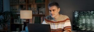 En mann i en stripete genser sitter ved skrivebordet sitt og ser på laptopen foran seg