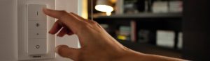 "Håndjusterer Philips smarte dimmer til LED-belysning, kontrollerer omgivelsesbelysningen i koselig stue med bokhyller."
